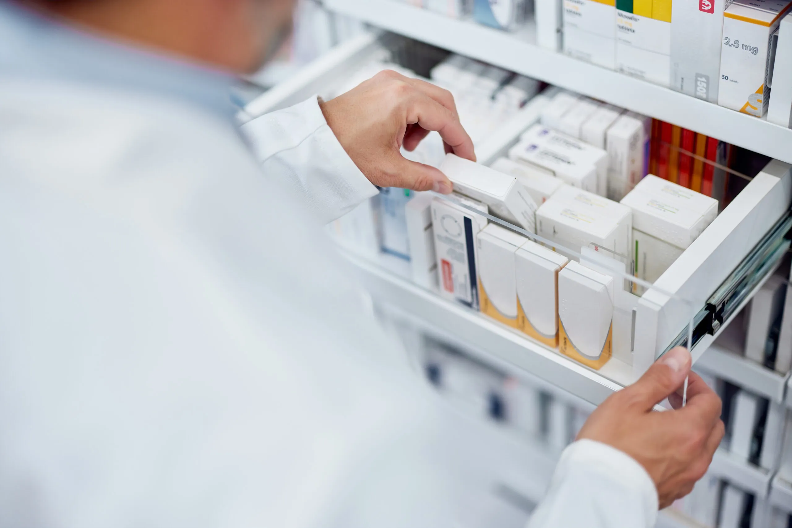 Apotheker greift nach einer Medikamentenpackung im Regal